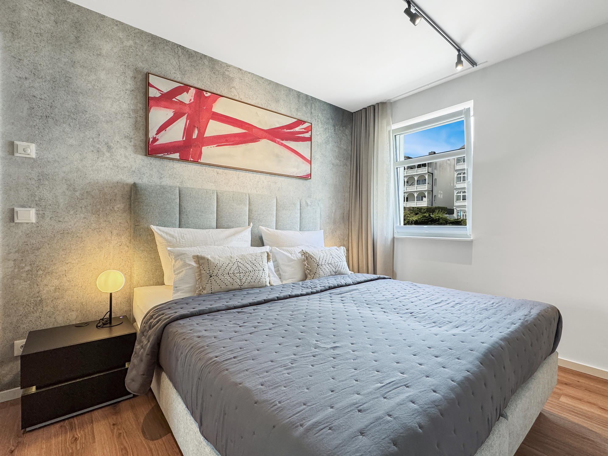 Schlafzimmer der Ferienwohnung Freiraum Fünf mit Hotel-Boxspringbett, Sichtbeton-Tapete und moderner Wandkunst