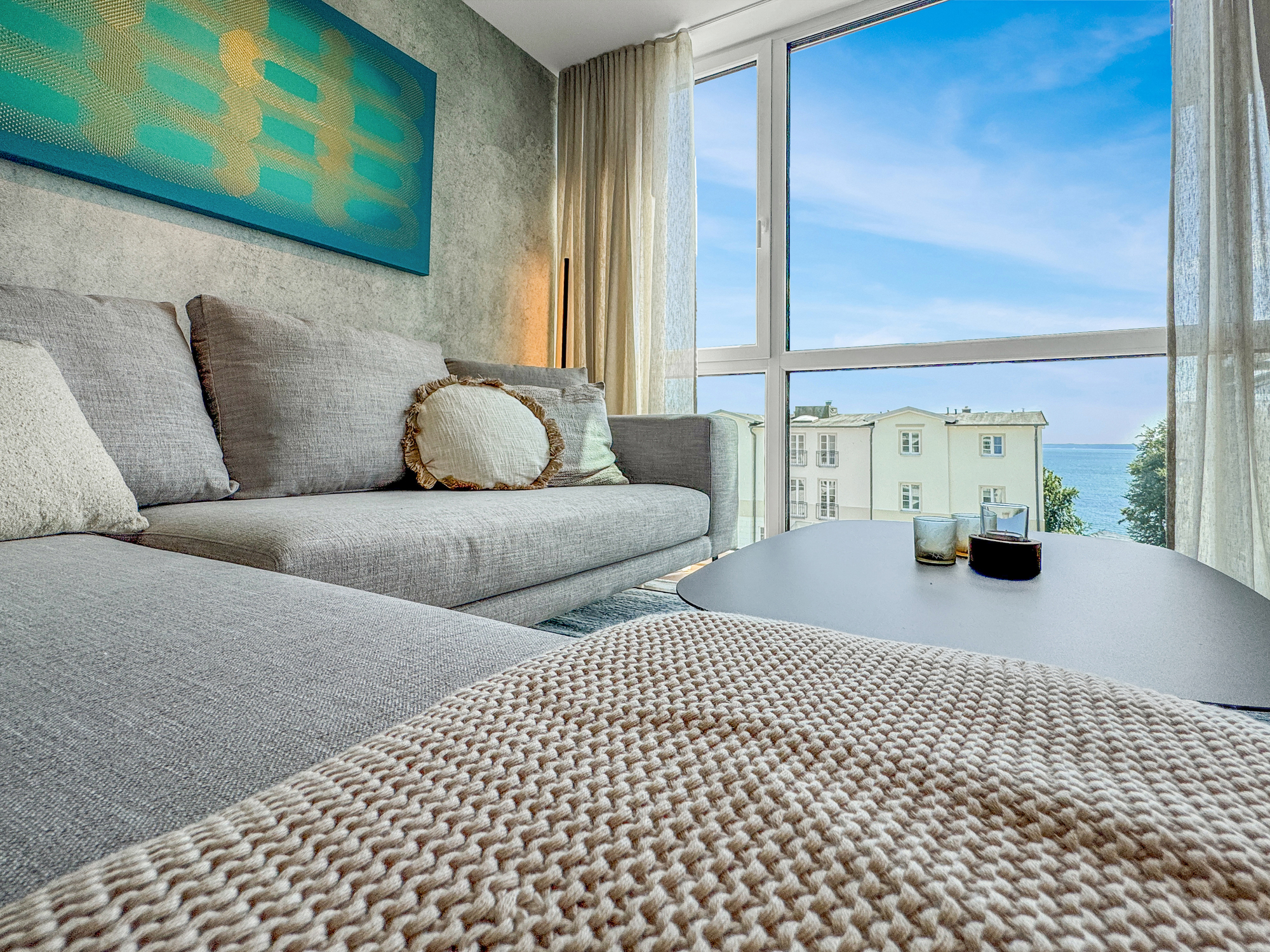 Hochwertiges Sofa vor farbenfroher Wandkunst und Blick auf die Ostsee von Sassnitz in einer Ferienwohnung